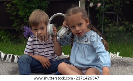 Two Happy Siblings boy ans girl listening to music on headphones outside in Garden. Children and technology. Brother and Sister. Love of music, dreams hobbies. Childhood, musicality, hobby. Friendship