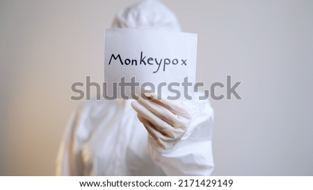 Isolated woman in protective suit, mask and goggles holds sheet of paper with inscription monkeypox and hands it to camera. Medium plan. Infectious disease. New pandemic in medicine. Blur effect