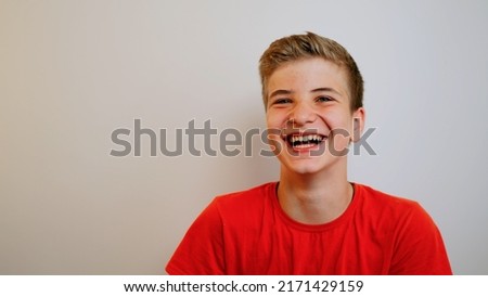 Happy positive teenage boy laughing at funny joke looking at camera on the wall background. Cheerful teen having fun, smiling face. Headshot close up portrait. Royalty-Free Stock Photo #2171429159