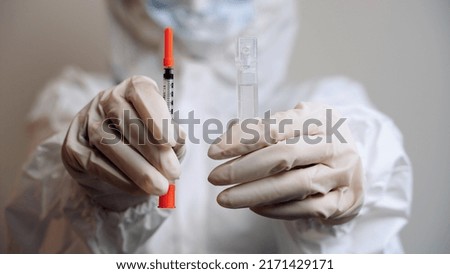 Isolated man in protective suit and gloves holding insulin syringe and ampoule with medication in hands close up. Vaccination against viral diseases. Immunization. Health care. Disease prevention