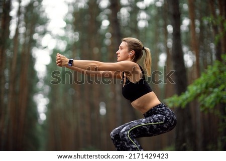 Athletic fit woman in sportswear squat training legs in forest. 