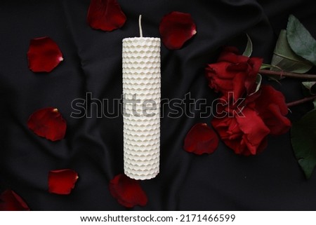Picture of conflagrant candle and wild rose on a black fabric background. Beeswax candle with rose petals