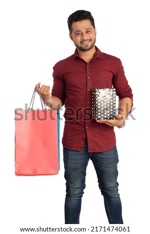 Young man holding and posing with shopping bags and gift boxes on a white background.