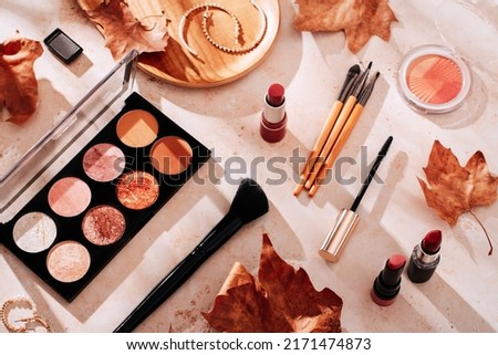 Beauty products and makeup, autumn leaves on beige background. Autumn skincare and autumn makeup concept.