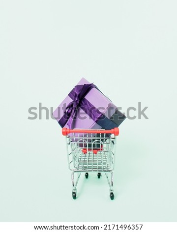 Purple gift box in shopping cart on pastel green background. Minimal buying present idea. Creative layout of shopping and giving concept.