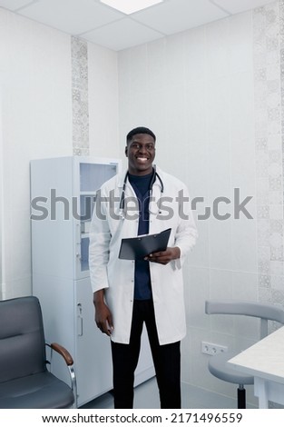 A picture of a handsome young doctor standing alone in his clinic.