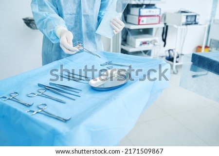 Doctor in surgical gown putting necessary tools into the tray Royalty-Free Stock Photo #2171509867