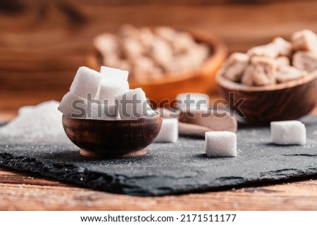 Bowl and scoop with white sand and lump white sugar on wooden background. Sugar cube. Make unhealthy nutrition, obesity, diabetes, dental care and much more.