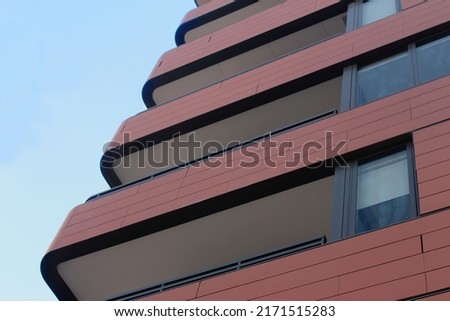 Close up of the corner of a building, showing balconies, windows. the structure is clad and has rounded corners