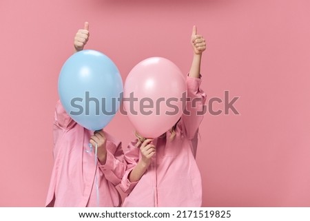 funny children hide behind balloons showing signs with their fingers and raising their hand up