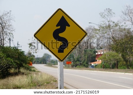 Yellow traffic sign  with twisty arrow symbol at rural road Thailand to warn drivers be careful when driving on twisty way road. Concept : Warning traffic sign for transportation.            