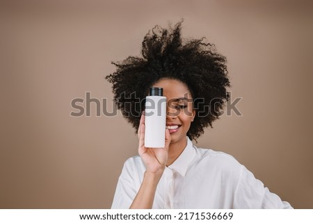 Beauty Latin woman with hairstyle. Brazilian woman. Holding blank shampoo packaging. Curly hair. Hair style. Pastel background.