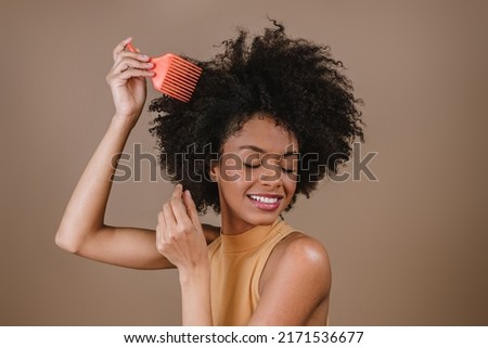 Young Latin woman combing hair. Fork for combing curled hair. Pastel background.