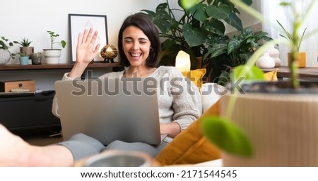 Panoramic image of young happy caucasian woman waving hand hello during online video call at home cozy living room.
