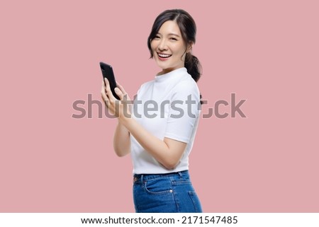 Attractive Young Asian woman pointing finger to mobile smartphone on isolated pink background. Royalty-Free Stock Photo #2171547485