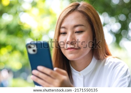 Portrait image of a beautiful young woman holding and using mobile phone in the outdoors
