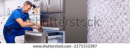 Mature Male Serviceman Repairing Refrigerator With Toolbox In  Kitchen Royalty-Free Stock Photo #2171553387