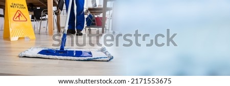 Janitor Cleaning Floor In Front Of Yellow Caution Wet Floor Sign