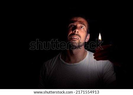Worried man looking up with a match in the dark. Concept of blackout. Royalty-Free Stock Photo #2171554913