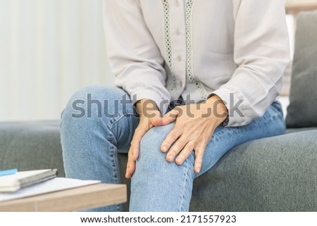 Body muscles stiff problem, senior woman pain in leg, suffering from knee ache from work, holding massaging rubbing knee joint injury, hurt or sore, painful sitting on sofa at home. Healthcare people. Royalty-Free Stock Photo #2171557923