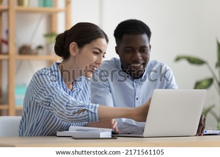 Two colleagues use laptop discuss corporate software. Female mentor provide help teach African newcomer explain corporate app. Communication, modern tech, client and saleswoman meet in office concept Royalty-Free Stock Photo #2171561105
