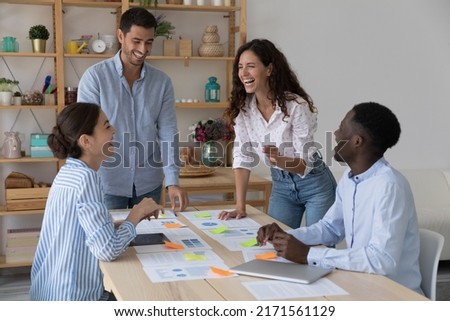Diverse millennial businesspeople, office employees cooperate, discuss project gathered together in boardroom feel enthusiastic communicates working on sales stats. Teamwork, workflow of staff concept Royalty-Free Stock Photo #2171561129