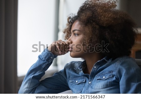 Close up side profile view face of African sad thoughtful teenager girl sit on sofa at home looking into distance feels unhappy, first unrequited love, teen relation problem, break up, worries concept Royalty-Free Stock Photo #2171566347