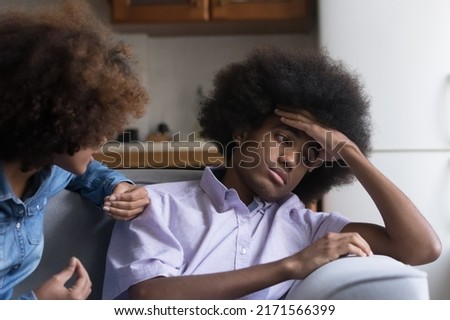 Teen African girl express her claim in aggressive manner to boyfriend sit nearby looks annoyed, ignoring girlfriend, feels disinterested to sort out their relationships. Bad relations, quarrel concept Royalty-Free Stock Photo #2171566399