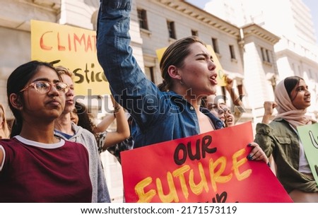Group of vibrant youth activists raising banners and shouting slogans during a climate change protest. Multicultural young people marching for climate justice and environmental sustainability.