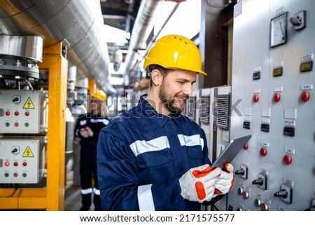 Professional industrial electrician in safety work wear checking power consumption on tablet computer. Royalty-Free Stock Photo #2171575577