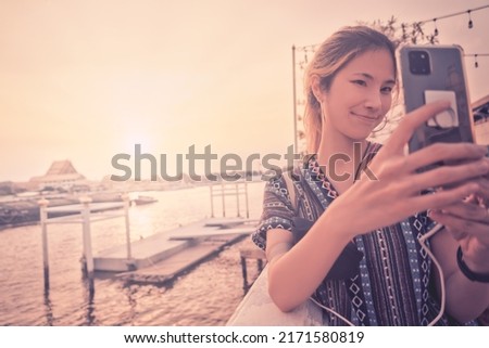 Asian woman traveler is taking selfie shot with the view of Chao Phraya river and temple, Bangkok Thailand