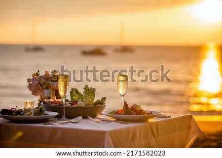 Romantic sunset dinner on the beach. Table honeymoon set for two with luxurious food, glasses of champagne drinks in a restaurant with sea view. Summer love, romance date on vacation concept. Royalty-Free Stock Photo #2171582023