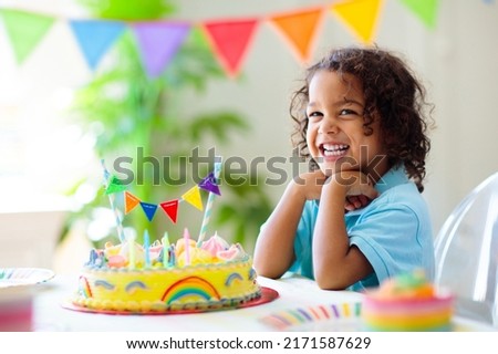 Kids birthday party. Children celebrate with colorful cake and gifts. Little curly boy blowing candles and opening birthday presents. Friends play with rainbow confetti. Party home decoration.