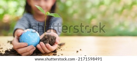 Banner of blurred  little girl is holding plant and globe model together, concept of ESG, environment, earth day, sustainability, world environment day, montessori education for kid and home school. Royalty-Free Stock Photo #2171598491