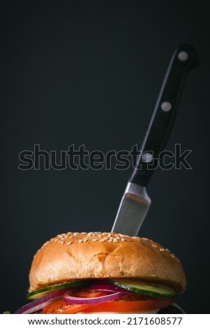 Big beef patty burger with cheese tomato purple onion cucumber and lettuce next to french fries on wooden black stand on black background