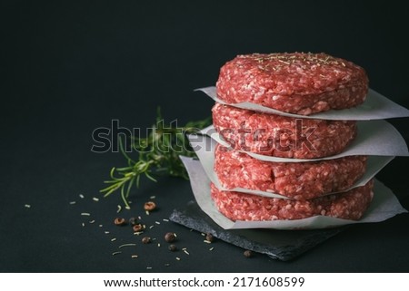 Raw ground beef burger patties separated by baking paper on a black background