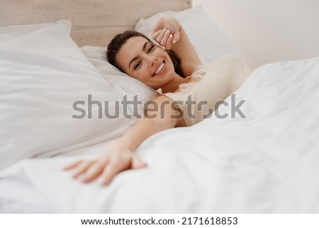 Smiling excited fun young woman in casual casual clothes lying in bed reach hand to camera you rest relax spend time in bedroom lounge home in own room house wake up dream be lost in reverie good day Royalty-Free Stock Photo #2171618853