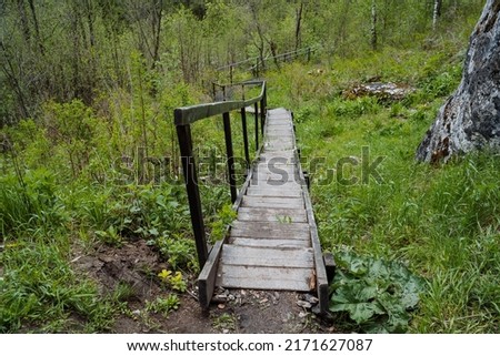 An old abandoned wooden staircase, steps from boards, a descent down the stairs with railings, a park for walking, a landscape in the forest. High quality photo Royalty-Free Stock Photo #2171627087