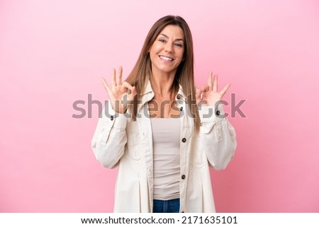 Middle age caucasian woman isolated on pink background showing ok sign with two hands