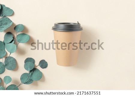 Top view of a Brown coffee paper cup. Mockup with black lid. Craft paper cup for coffee or tea on beige background. Zero waste, plastic free concept. Disposable Recycled cup. Coffee to go, eucalyptus.