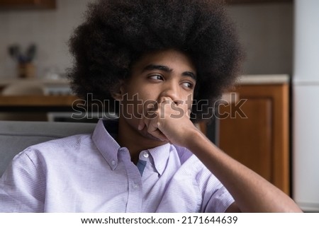 Close up face pensive African teenage 18s guy sit at home alone, looks deep in thoughts and pensive thinks over life concerns or unrequited love. Teen-age relations problems, break up, worries concept Royalty-Free Stock Photo #2171644639
