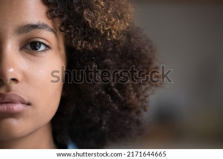 Close up cropped half non-make up face view of young 20s gorgeous African beautiful girl pose look at camera. American serious cute curly-haired teenager portrait, gen Z person, natural beauty concept