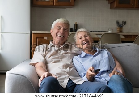 Laughing older couple relax on sofa spend carefree weekend together at home, hold remote control switch channels enjoy movie, watch favourite funny TV show use online stream services. Leisure concept Royalty-Free Stock Photo #2171644669