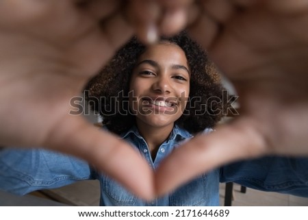Beautiful African teenage girl make heart symbol with joined fingers in front of camera, close up cropped view face through affection sign. I Love You declaration, sincere feelings, first love concept Royalty-Free Stock Photo #2171644689
