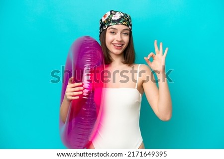 Young Ukrainian woman holding air mattress isolated on blue background showing ok sign with fingers