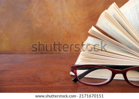 open book and glasses lie on a wooden brown table
