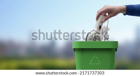 Woman putting an old appliance in the trash bin, recycling concept, green landscape in the background Royalty-Free Stock Photo #2171737303