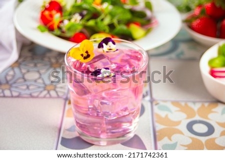 Glass of pink violet purple cocktail decorated flowers viola pansy