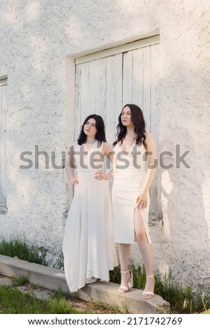 two young girls in white dress on background old white wall