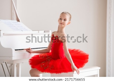 cute little girl dreams of becoming professional ballerina. In a white room, he stands at the piano in bright red pack. Vocational school student.